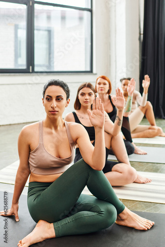 diverse group of multiethnic female friends in sportswear meditating while sitting in lord of fishes pose and looking away during yoga class in gym  wellness and mental health concept