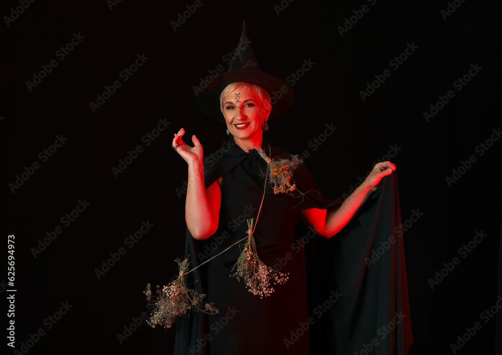 Mature witch with herbs on dark background