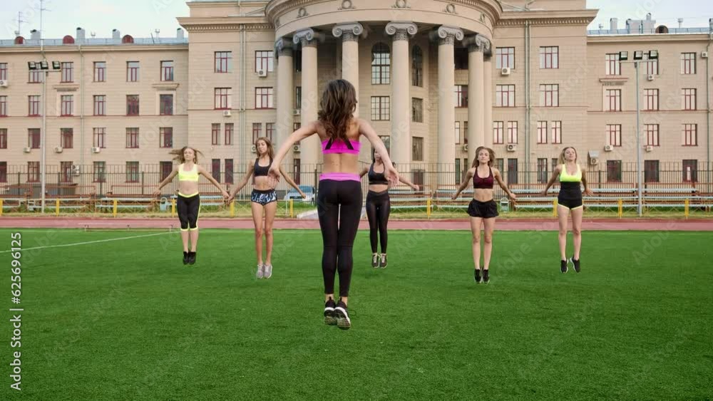 Sportive and smiley. Group of athletic young women in sportswear doing physical exercises with coach in green summer park of the university. Team of Girls doing sport and physical exercises outdoor Sportive and smiley. Group of athletic young women in sportswear doing physical exercises with coach in green summer park of the university. Team of Girls doing sport and physical exercises outdoor