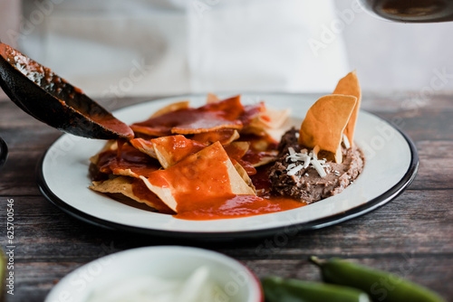 Fototapeta Naklejka Na Ścianę i Meble -  Mexican woman hands preparing chilaquiles with red sauce and eating traditional mexican food for breakfast in Mexico Latin America