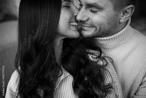 Black and white photo of happy young couple in love is hugging, kissing and smiling together celebrating Valentine's day at home. Man and woman enjoying spending time together, relaxing on date