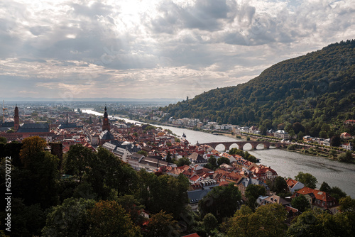 Aerial drone view over famous city of Heidelberg Germany with bridge on river Neckar. Dramatic cloudy sky with sunbeams over old town and mountains