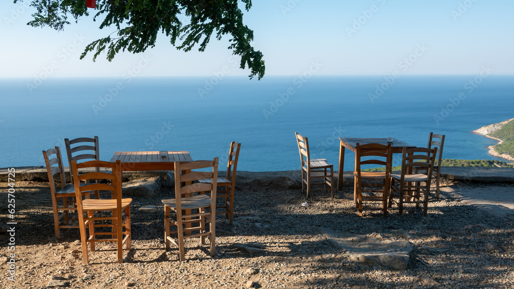 Gokceada (Imbros) coastline and a cute village tea garden view with wooden chairs and table. Tepeköy village, Çınaraltı-Pinarbasi location, Aegean Turkey