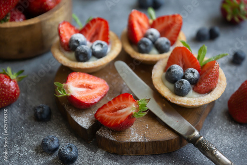 Fruit dessert tarts with cream, strawberry and blueberry on wooden table