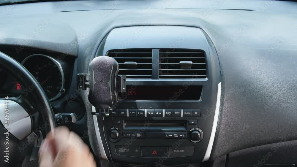 Hands of a young European men sitting in a car with a black interior, attaches a phone holder to the dashboard of the car