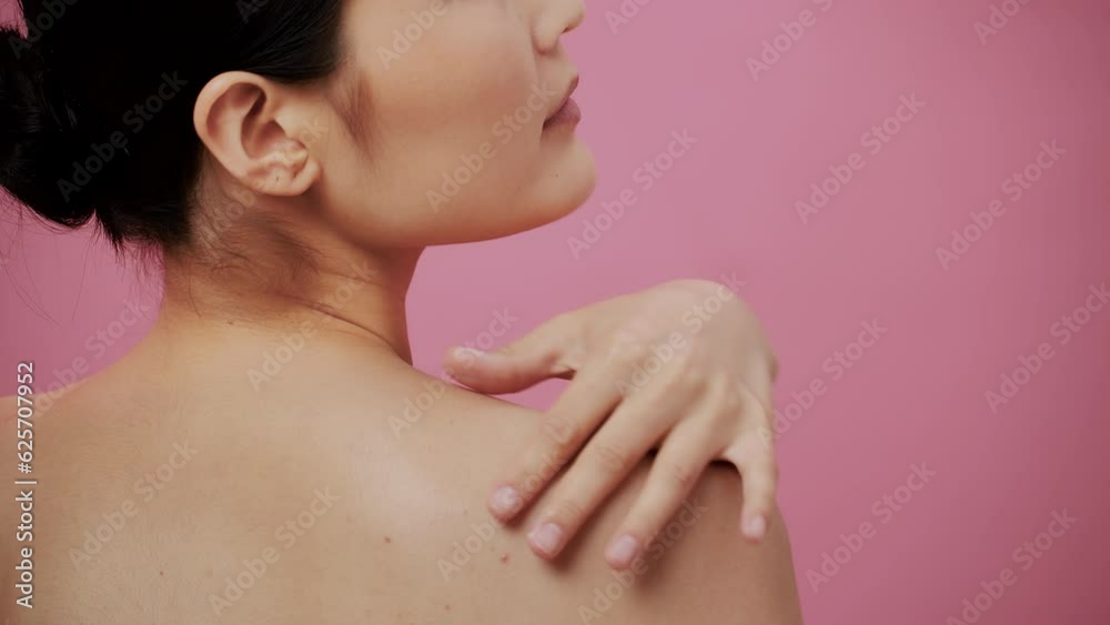 Beautiful female model with perfect clean fresh skin. Close-up of a beauty asian young woman massages and apply a cream on her shoulder, on pink background. Skin care treatment concept Beautiful female model with perfect clean fresh skin. Close-up of a beauty asian young woman massages and apply a cream on her shoulder, on pink background. Skin care treatment concept