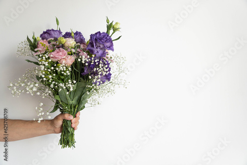 Mans hand holds bouquet of beautiful violet and pink flowers on white background.