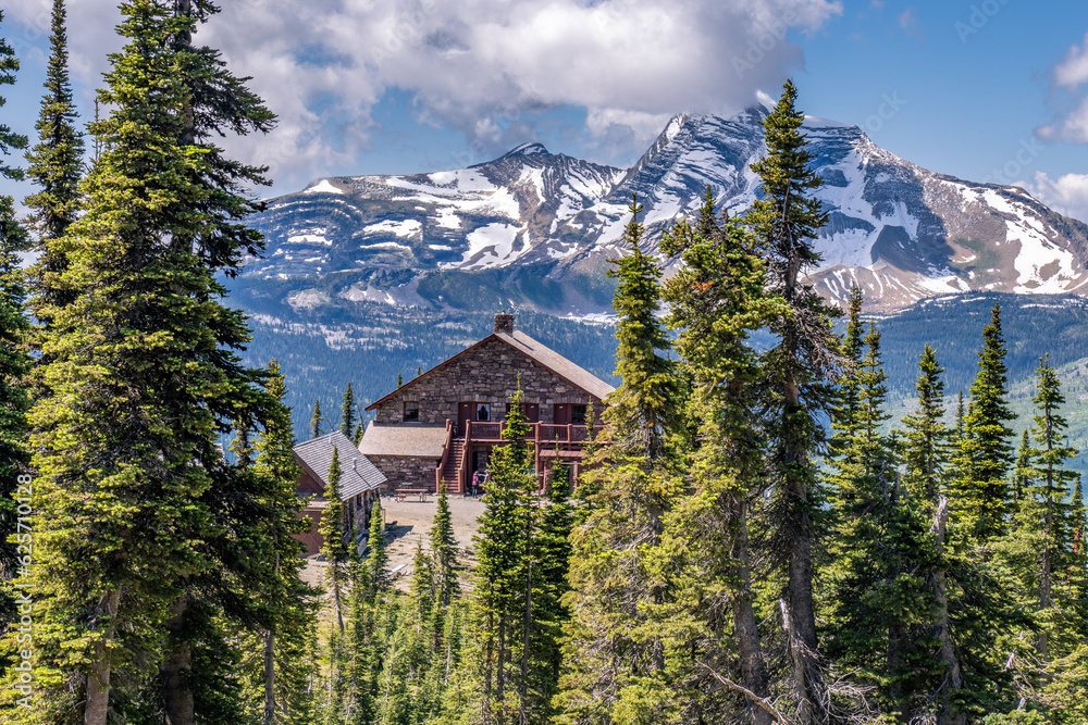 An historic stone structure nestle on a hill surrounded by mature pine trees and a rugged mountain in the background, Granite Park Chalet, Glacier National Park, Montana