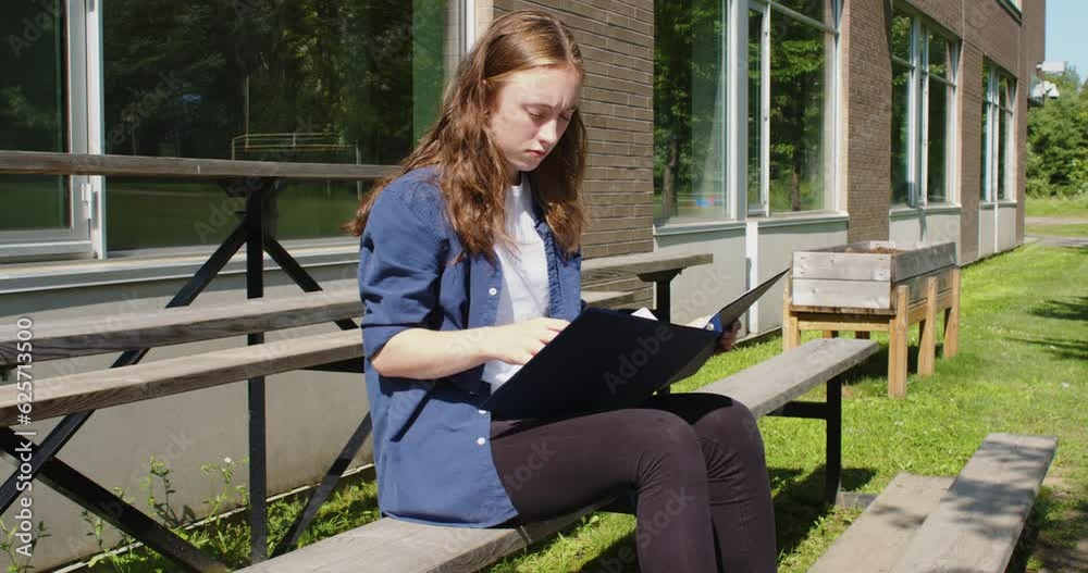 Frustrated student sitting on bleachers while studying in front of a school