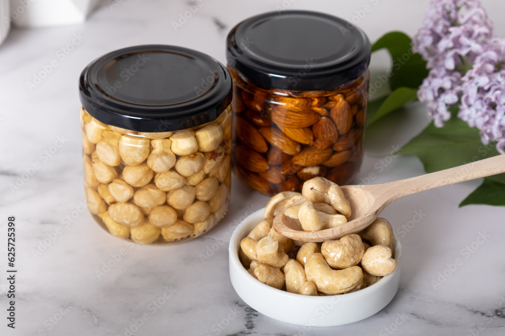 Сashew in honey with spoon with glass jars on marble background. Сashew in honey with spoon with glass jars on marble background.