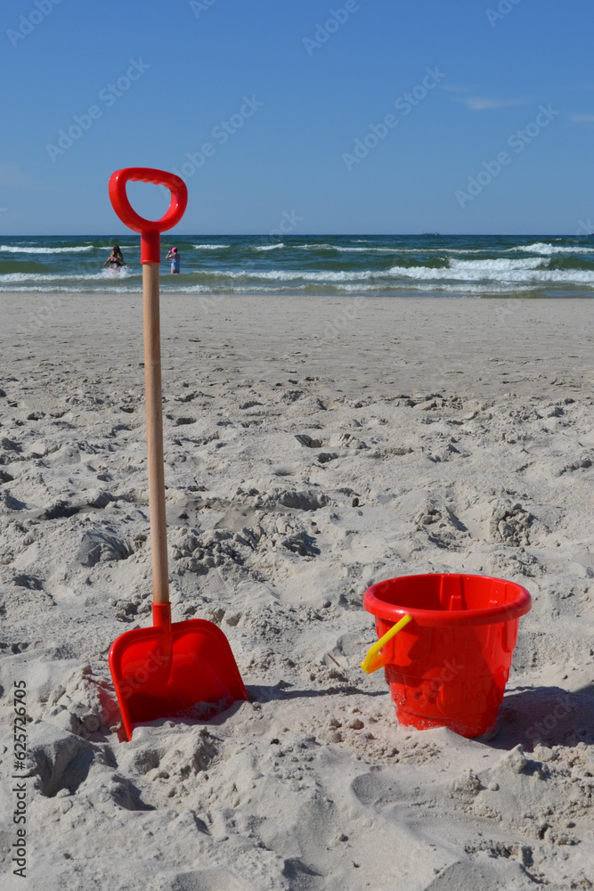 Plastic red bucket and shovel on sandy beach. Children's sand play equipment Plastic red bucket and shovel on sandy beach. Children's sand play equipment