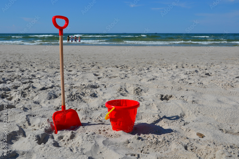 Plastic red bucket and shovel on sandy beach. Children's sand play equipment Plastic red bucket and shovel on sandy beach. Children's sand play equipment