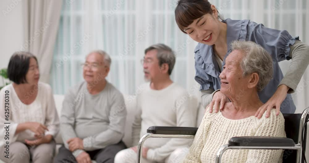 A beautiful kindness young Asian nurse stand behind the old woman in wheelchair and massage her shoulders and they talking with a smile at nursing home. the other senior chatting together on the back. A beautiful kindness young Asian nurse stand behind the old woman in wheelchair and massage her shoulders and they talking with a smile at nursing home. the other senior chatting together on the back.