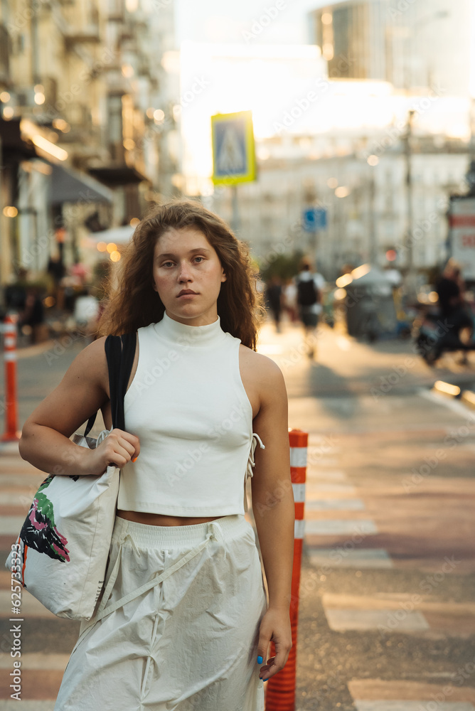 A chic girl wearing white clothes and sporting curly hair on the city streets.