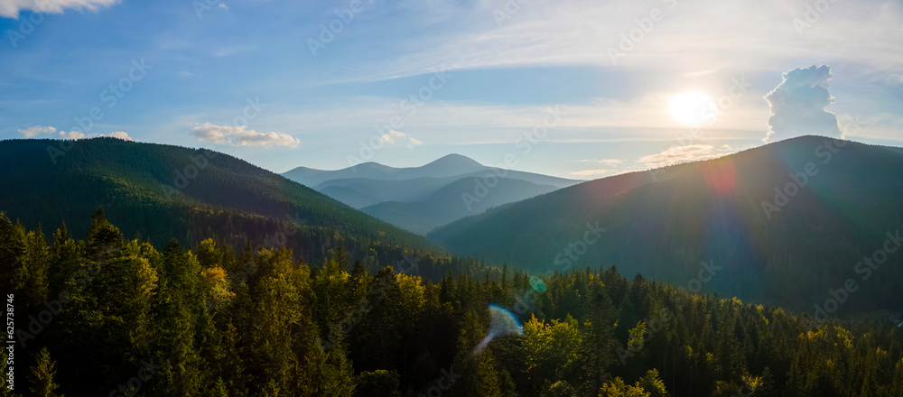 Obraz premium Aerial view of bright foggy morning over dark hills with mountain forest trees at autumn sunrise. Beautiful scenery of wild woodland at dawn