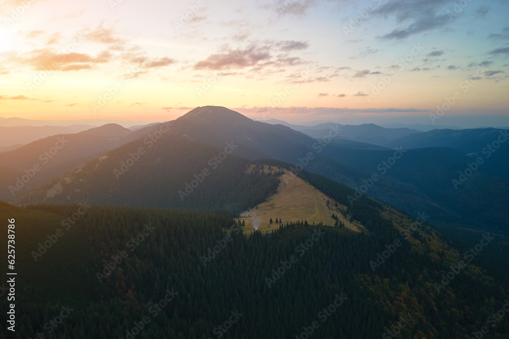 Aerial view of bright foggy morning over dark peak with mountain forest trees at autumn sunrise. Beautiful scenery of wild woodland at dawn