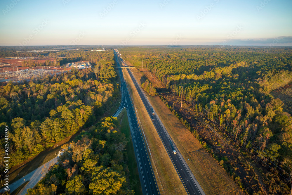 View from above of busy american highway with fast moving traffic between autumn woods. Interstate transportation concept