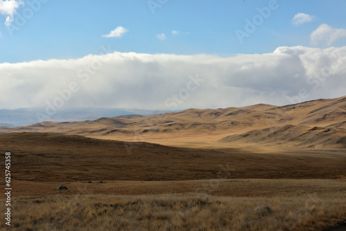 High hills on the edge of the autumn steppe with dried grass in the shade from low clouds on a sunny day.