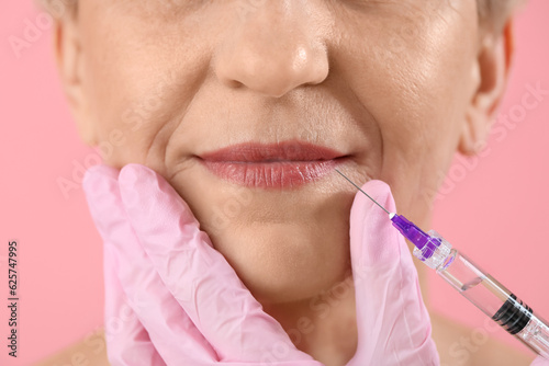 Mature woman receiving lip filler injection on pink background  closeup