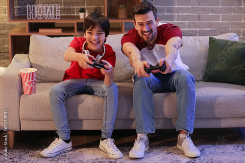 Little boy with his father playing video game at home in evening