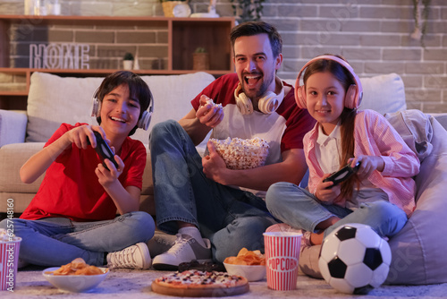 Papier peint Father eating popcorn while his little children playing video game at home in ev