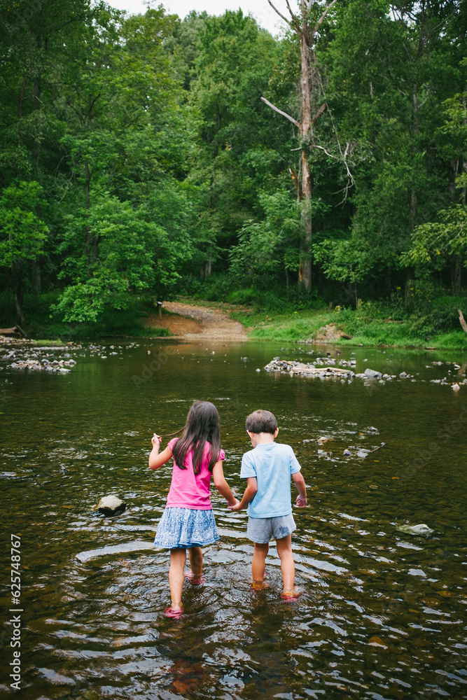 Two children holding hands wade into the Eno River in Durham, North Carolina Two children holding hands wade into the Eno River in Durham, North Carolina