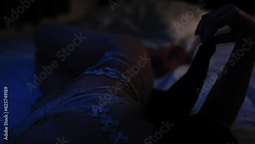 A beautiful woman wearing white lingerie in a dark bedroom removing her black robe and revealing her sexy body