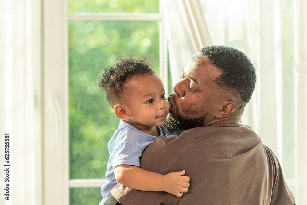 Fototapeta premium Happy african black parents dad father throw baby son on piggyback and neck riding teasing fun near window. Black baby son and daddy enjoy teasing kiss cheek and neck riding at window light