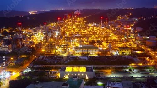 Aerial hyperlapse over a CPC oil refinery plant in a petrochemical industrial estate, with huge storage tanks and pipelines throughout the factory and the lights glowing at dusk in Taoyuan, Taiwan