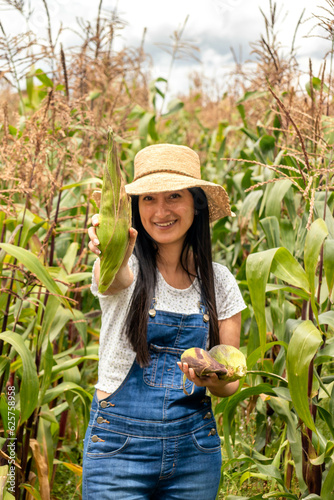 mujer sonrriendo en un día soleado mostrando en primer plano un choclo o maiz tierno, mujer con sombreo de paja estilo campesino  photo