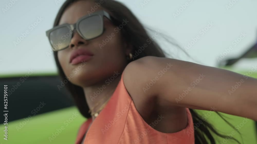 Swarthy young woman in green dress and sunglasses sitting next to expensive green sports car Swarthy young woman in green dress and sunglasses sitting next to expensive green sports car