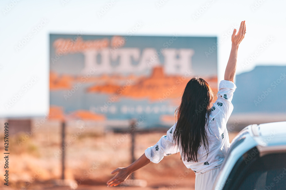 Beautiful woman on her trip by the car on the background of Welcome to Utah state border sign right in the Monument Valley