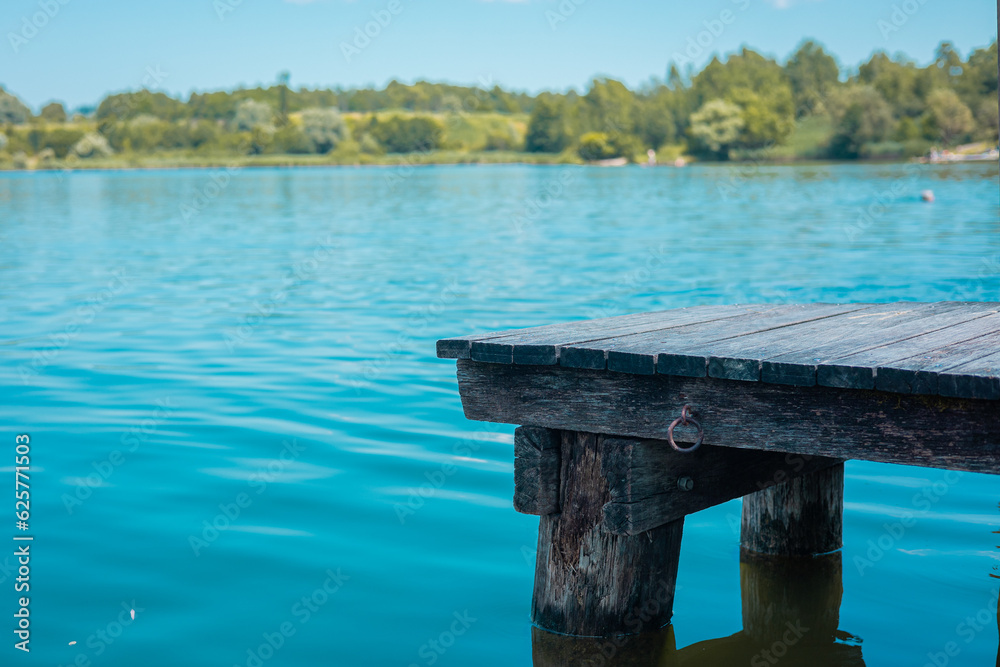 Wooden pier on two masts and crystal blue waters of lake in kocevje or Kocevsko jezero, with tranquil bathing water visible on a summer day. Great cooling off in summer.