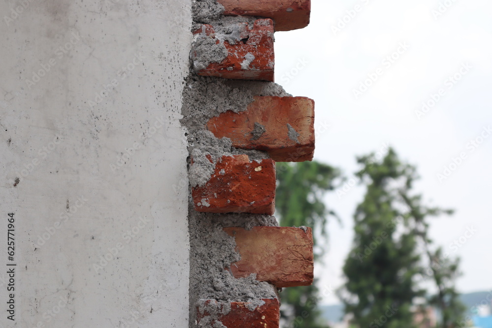 An under construction white wall with red bricks on its end and few trees in a blurred background An under construction white wall with red bricks on its end and few trees in a blurred background