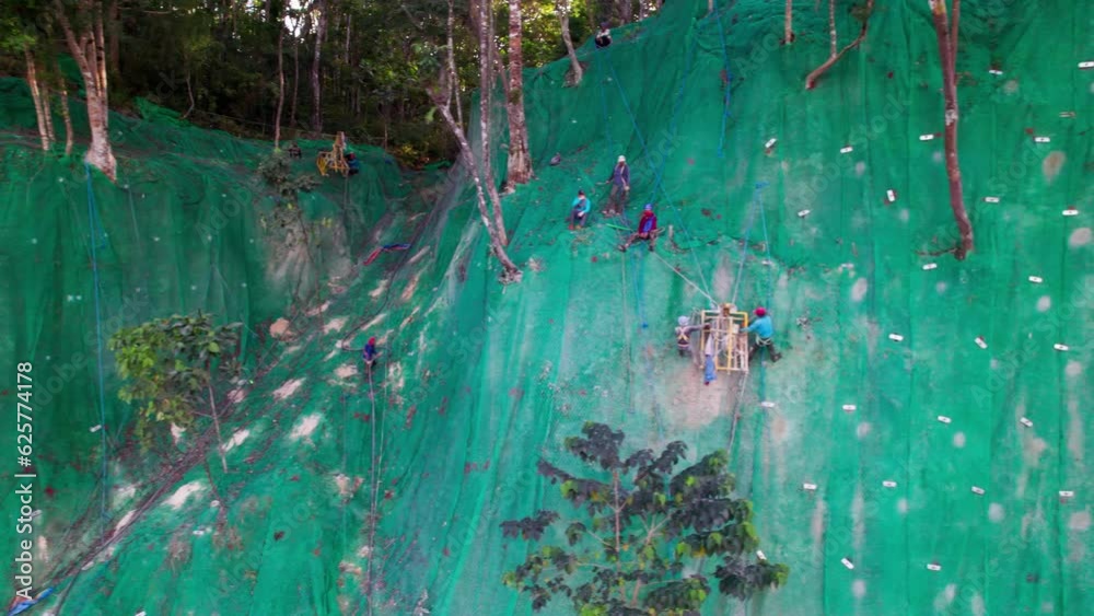 Ouvriers escaladant une falaise recouverte d'un filet vert sur un chantier de Bohol aux Philippines, Asie