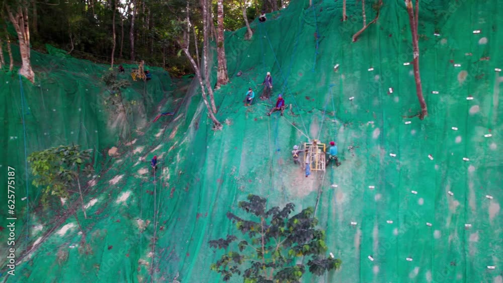 Ouvriers escaladant une falaise recouverte d'un filet vert sur un chantier de Bohol aux Philippines, Asie