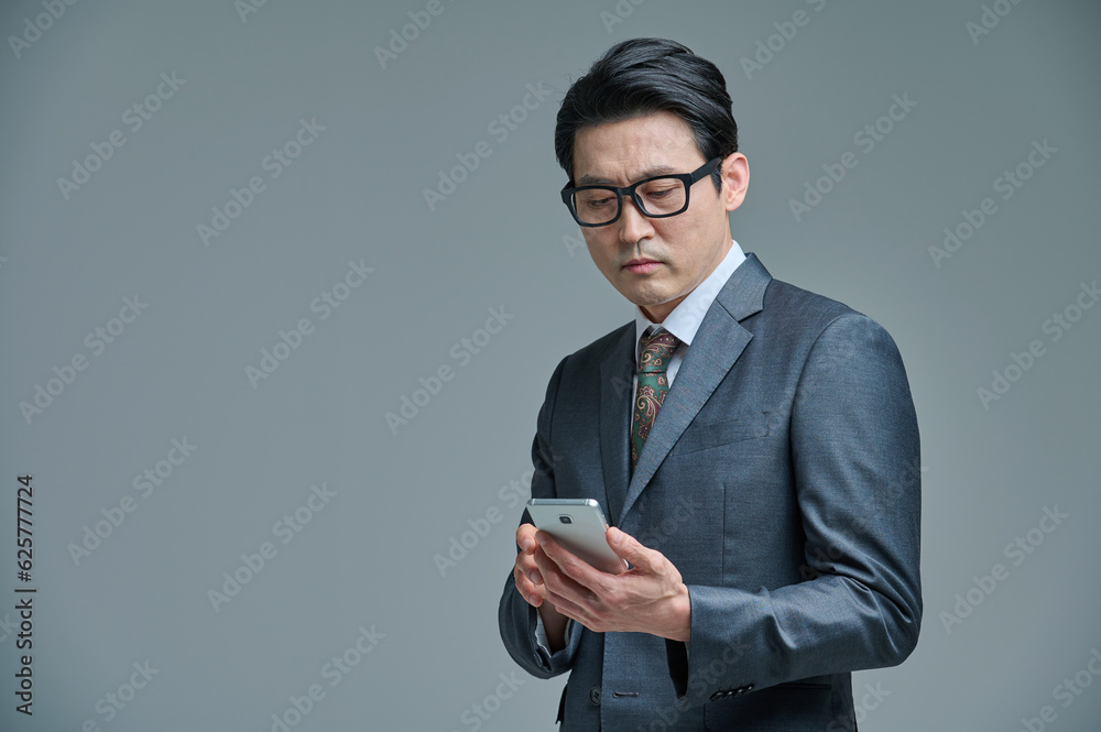 A middle-aged office worker wearing a suit is wearing glasses and holding a smartphone and making various emotional expressions. A middle-aged office worker wearing a suit is wearing glasses and holding a smartphone and making various emotional expressions.
