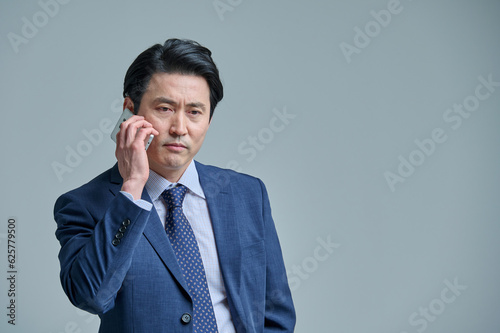 A middle-aged office worker in a suit is holding a smartphone and making various emotional expressions.