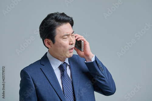 A middle-aged office worker in a suit is holding a smartphone and making various emotional expressions.