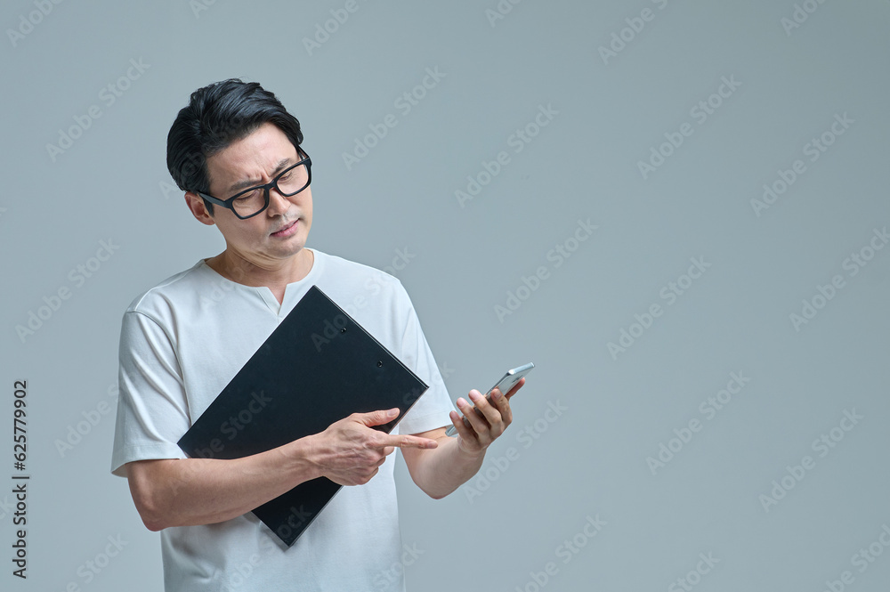 A middle-aged office worker wearing casual clothes and glasses is holding a smartphone and files and making various emotional expressions. A middle-aged office worker wearing casual clothes and glasses is holding a smartphone and files and making various emotional expressions.