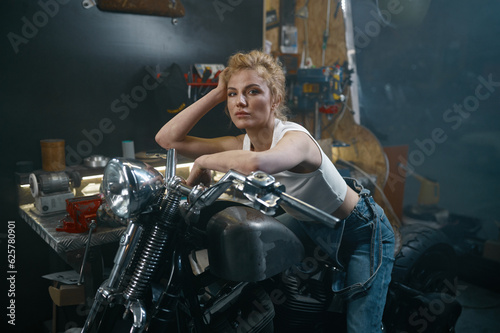Portrait of beautiful woman biker sitting on motorcycle in garage