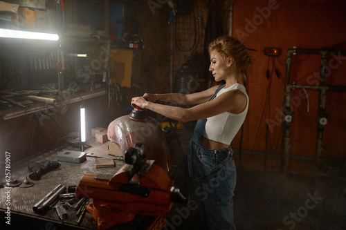 Young woman doing hard job at motorcycle garage using grinder