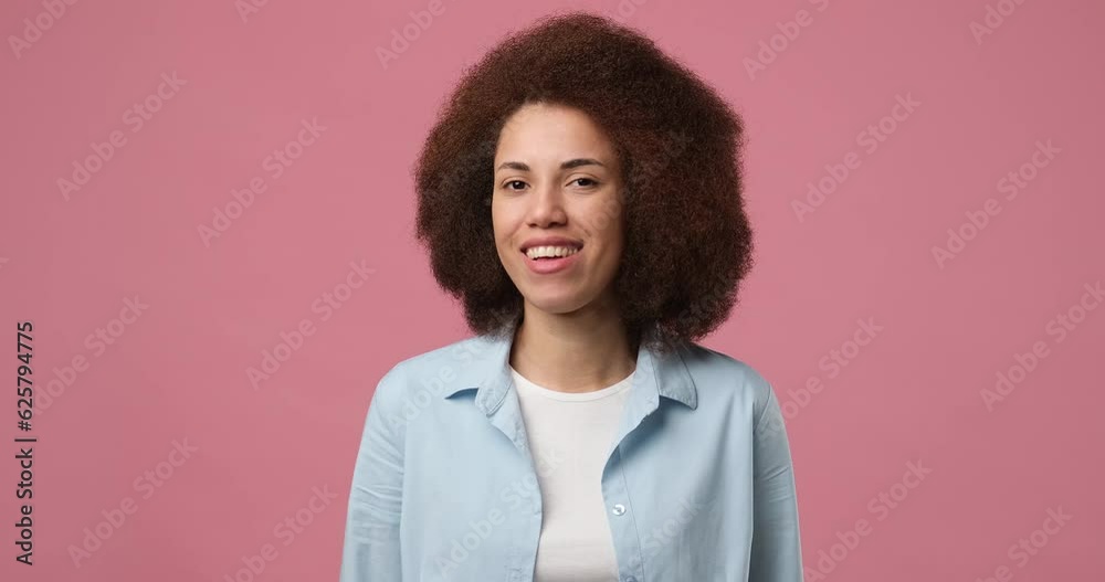 Smiling attractive african american woman winks looking at camera standing over pink studio background Smiling attractive african american woman winks looking at camera standing over pink studio background