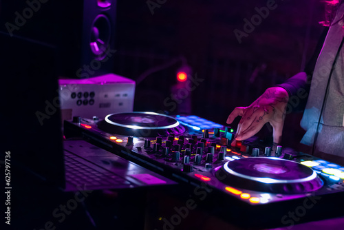 Close up of DJ hands playing various track controls on the DJ mixing console at the nightclub party.