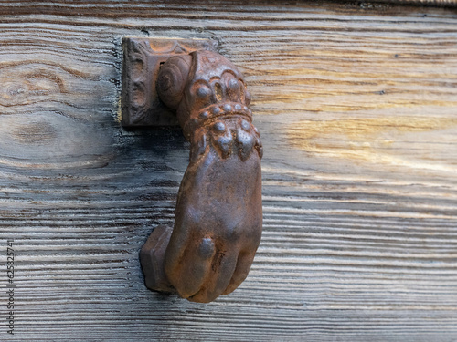 Antigua puerta de madera con aldaba de fundición, en el pueblo mallorquín de Deia, con forma de mano sobre la madera envejecida mostrando su textura photo