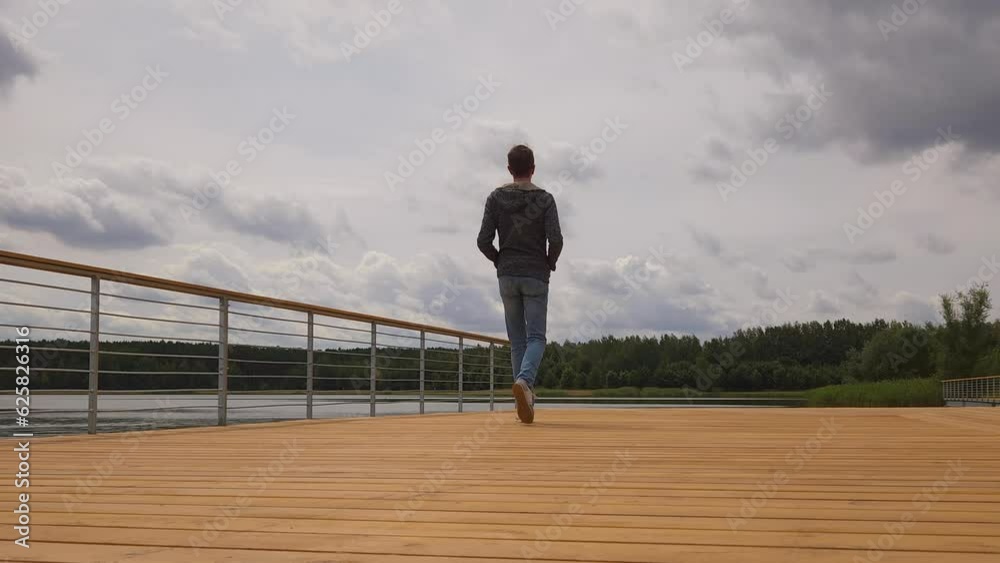 Man walks along pier, stops at edge and looks at water Man walks along pier, stops at edge and looks at water
