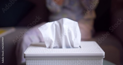 White paper tissue in a metal container box standing on a table outdoors in street sunny restaurant. Female hand takes one paper napkin blowing by the wind photo