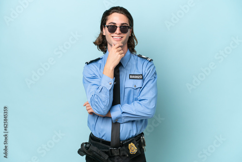 Young police caucasian man isolated on blue background with glasses and smiling