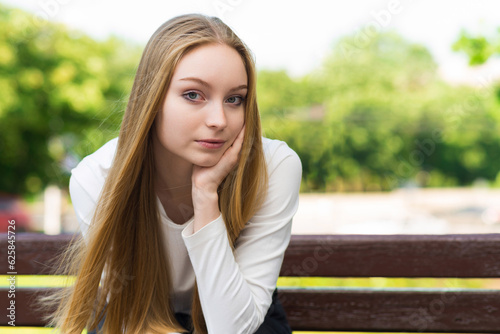 Portrait of a girl sitting on a bench in a green park on a sunny day. Rest concept.