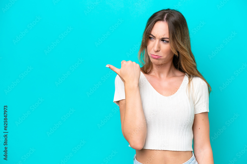 Young caucasian woman isolated on blue background unhappy and pointing to the side Young caucasian woman isolated on blue background unhappy and pointing to the side